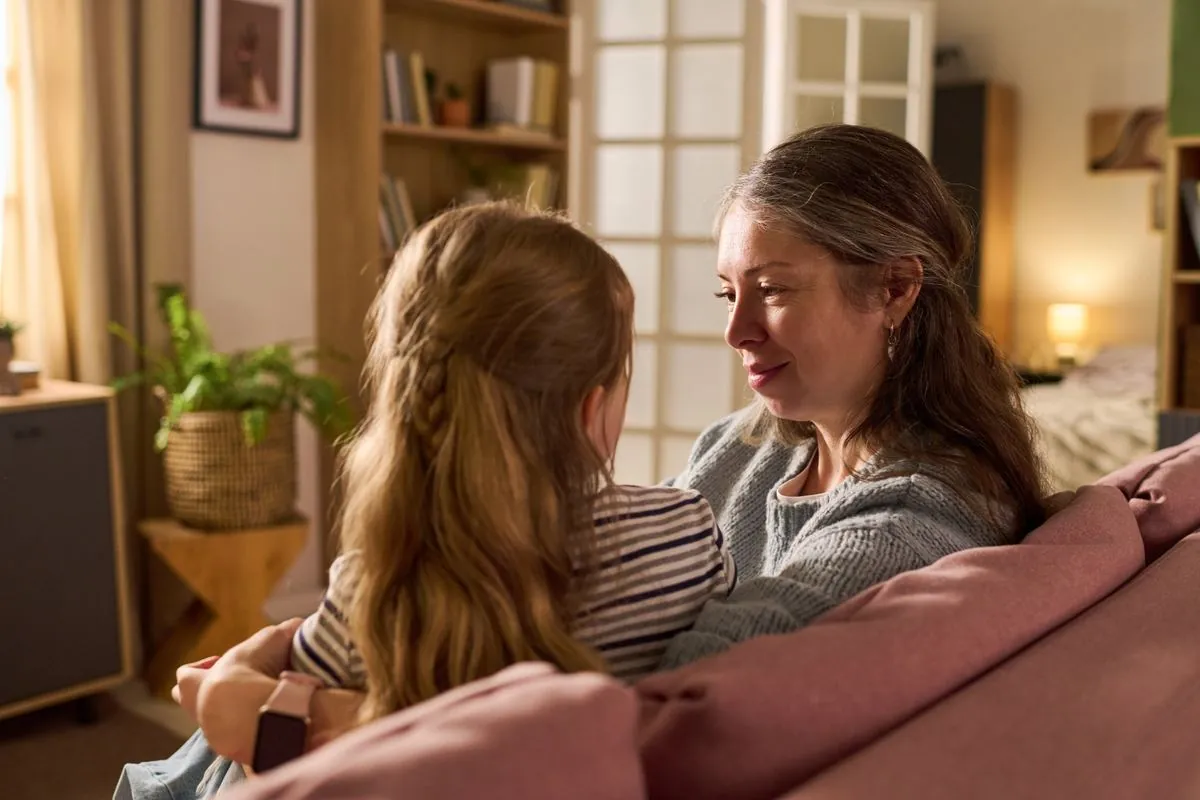 A carer listening closely to a young girl on the sofa