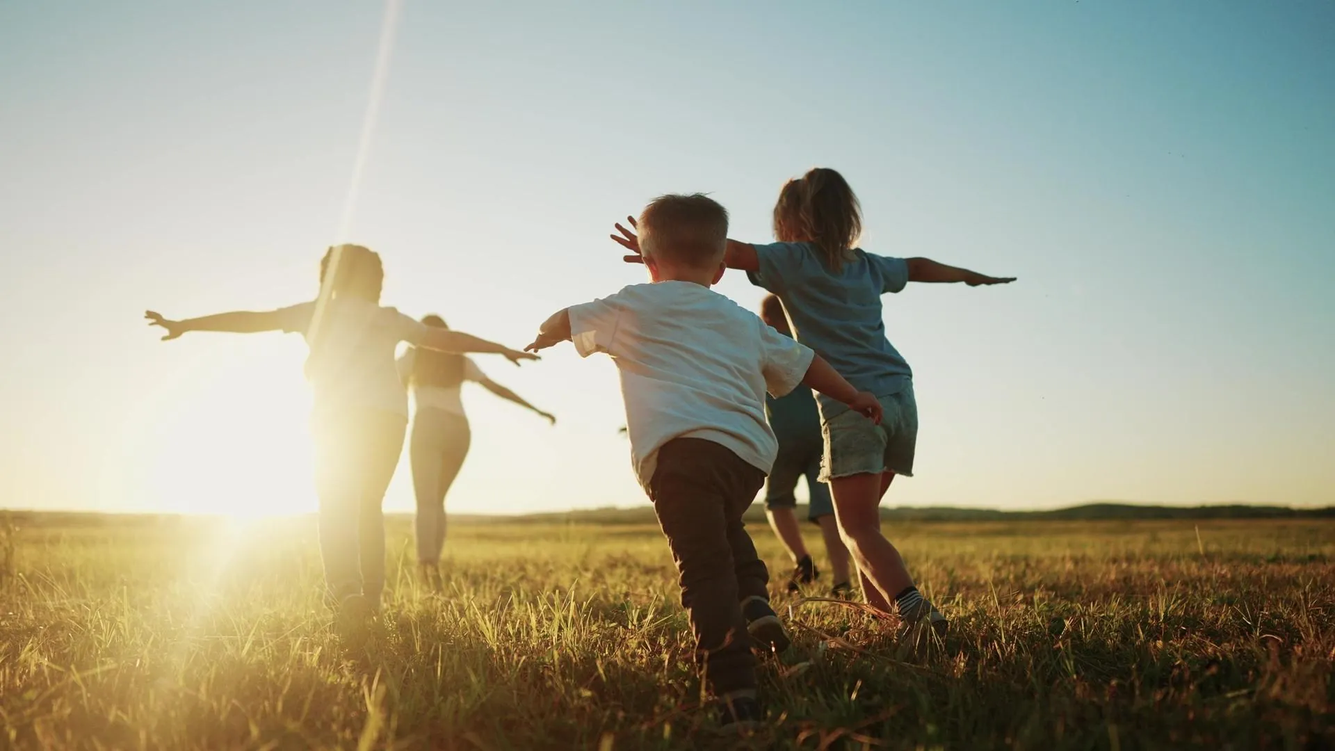 Children running across a field at sunset with their arms out like aeroplanes