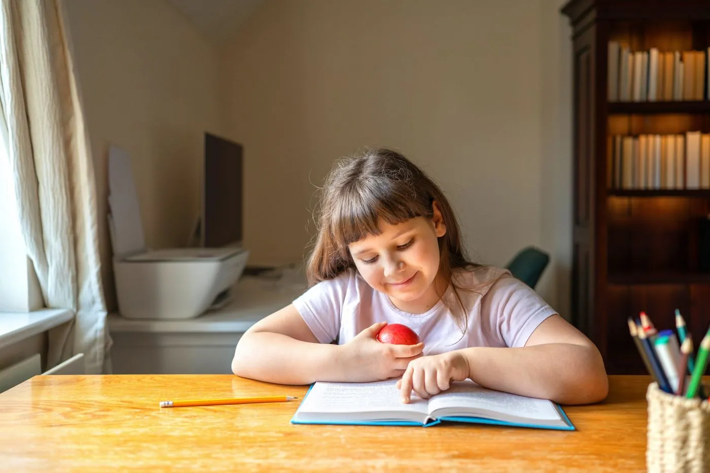 A young girl reading a book at a study desk at home