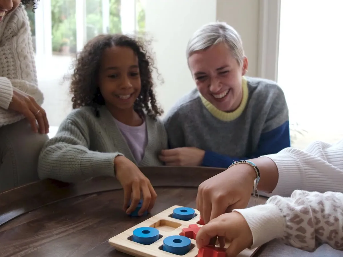 A carer laughing with children as they play a board game at the table